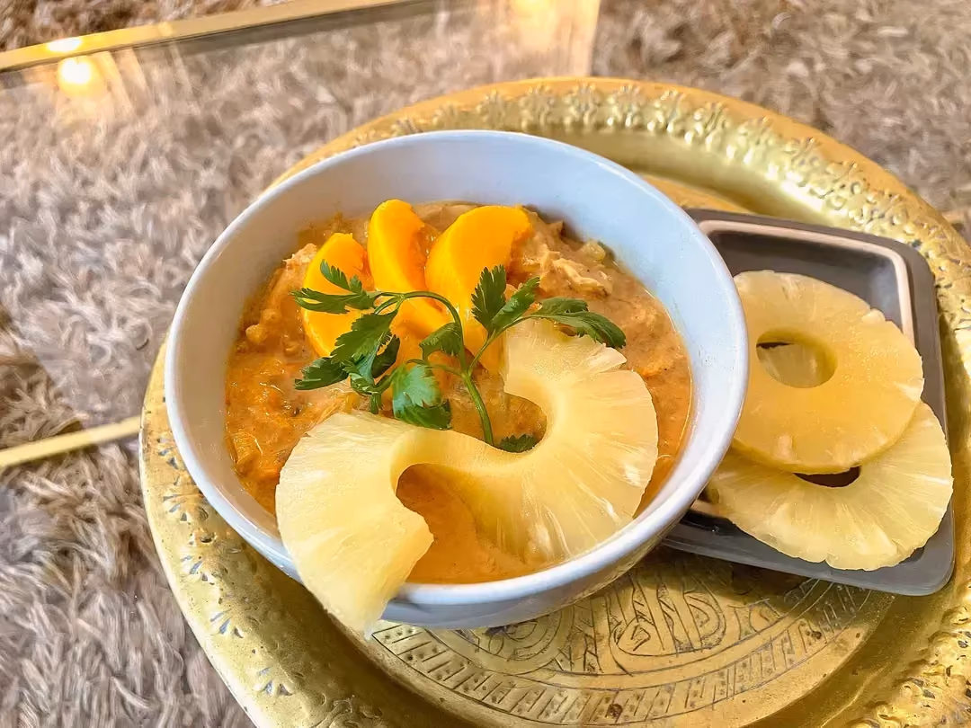 Le curry est présenté dans un bol avec des tranches d'ananas et de pêches sur le dessus, le tout posé sur un plateau de couleur doré.
