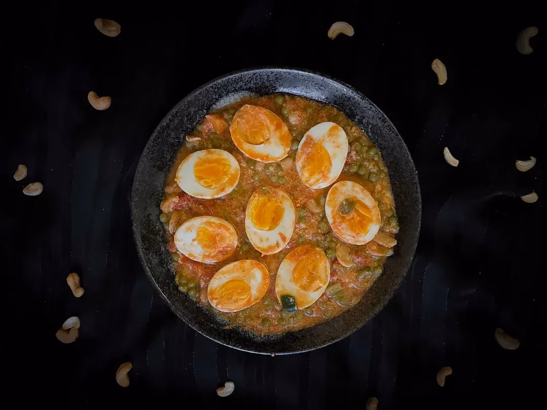 In a small blue bowl, there are four curried eggs cut in half and peas.