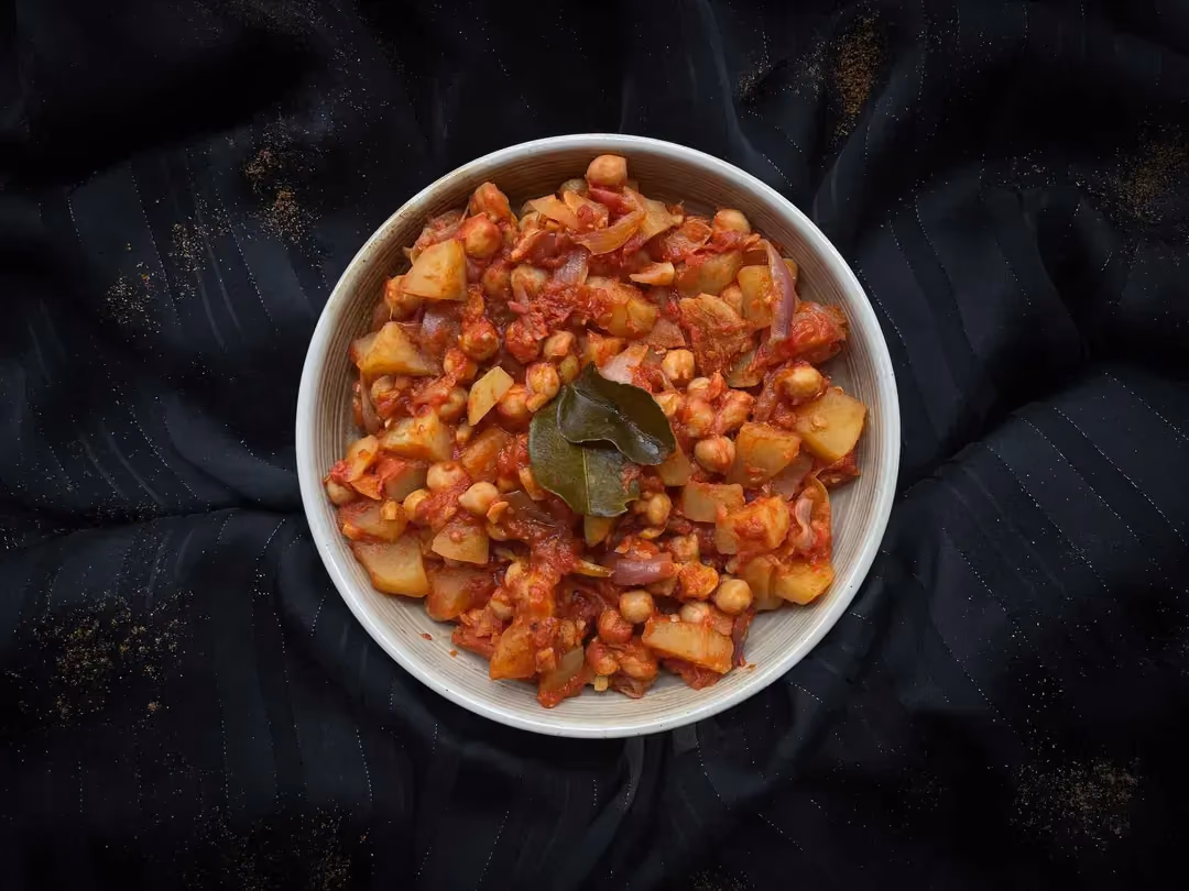 Dans un large bol se trouve le curry de pois-chiche et pommes de terre, accompagné de riz et de quelques tranches triangulaires de pain naan.