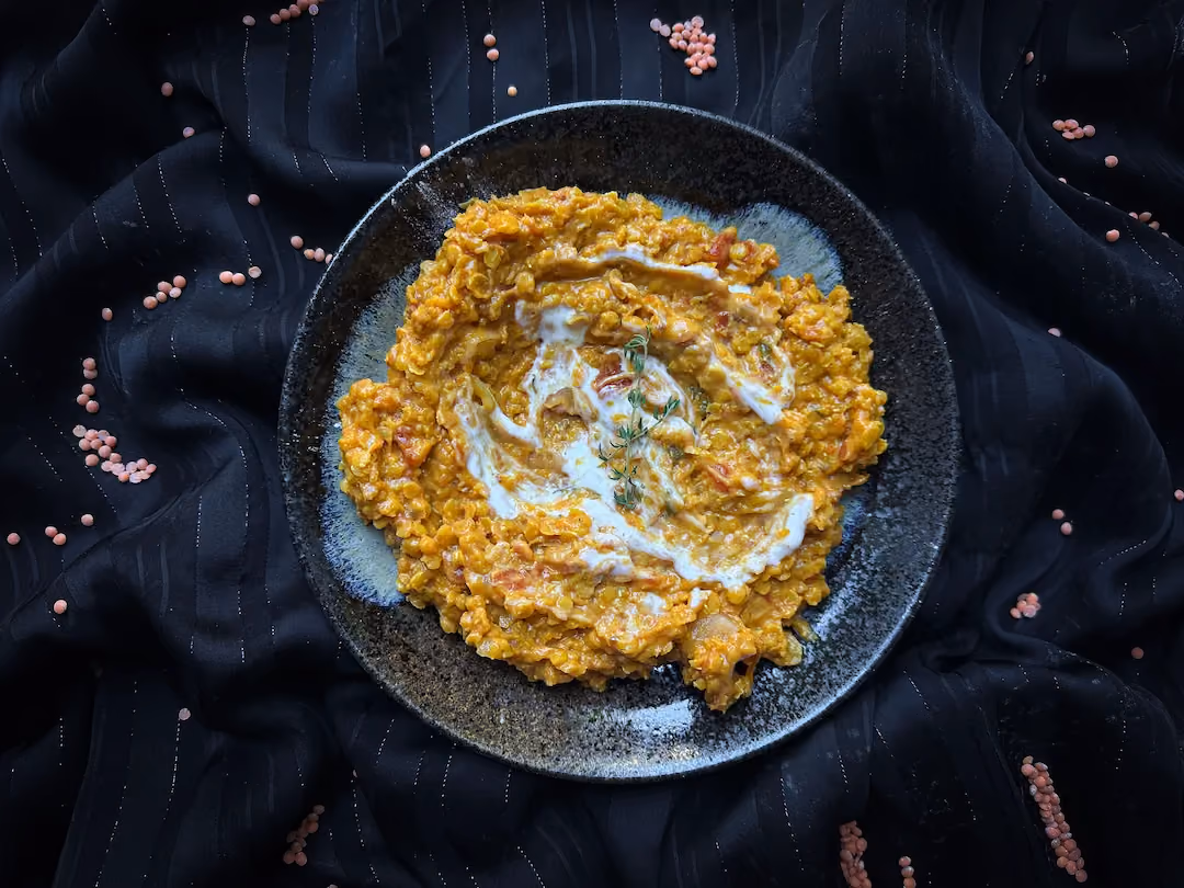 Dans une assiette creuse de couleur bleu et noir, le dahl de lentilles corail se présente sous la forme d'une sorte de purée de couleur safran.