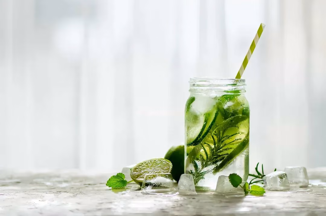 Dans un pot en verre se trouve les tranches de pommes vertes, le citron vert et le basilic. Quelques glaçons accompagnent le détox water.