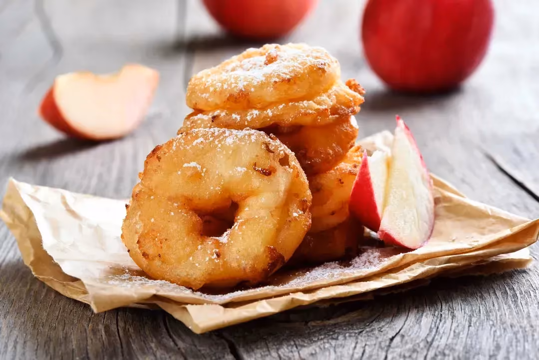 Quelques donuts reconnaissables avec leur trou au centre sont posés sur un sac en papier. Deux belles pommes rouges sont visibles également.