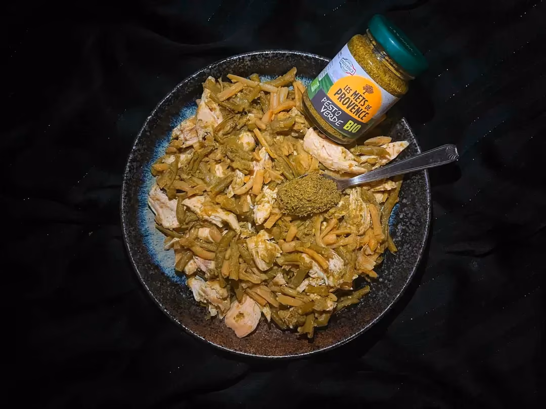 Le duo de haricots verts et poulet à la sauce pesto est présenté dans un petit saladier. Un pot de sauce pesto et une petite cuillère sont visibles