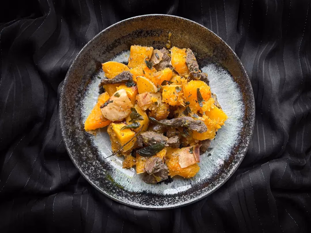 Un saladier de taille moyenne reçoit la recette d'émincés de boeuf, les gros cubes de courge butternut et sirop d'érable.