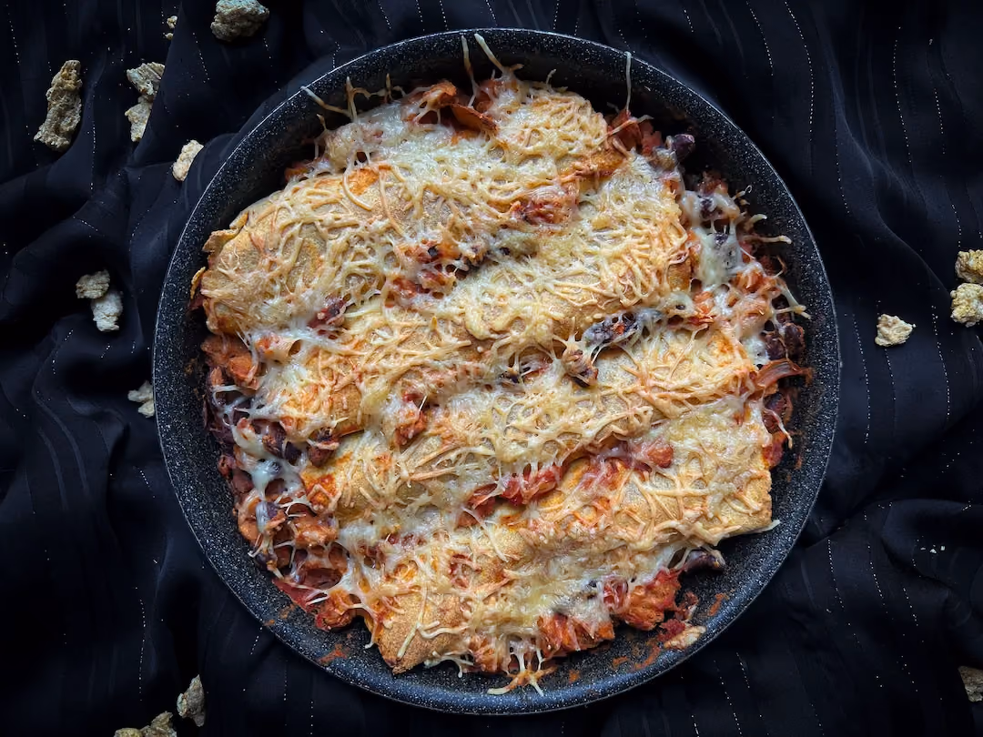 These vegetarian enchiladas with cheese, kidney beans, and soy protein are presented in a black baking dish.