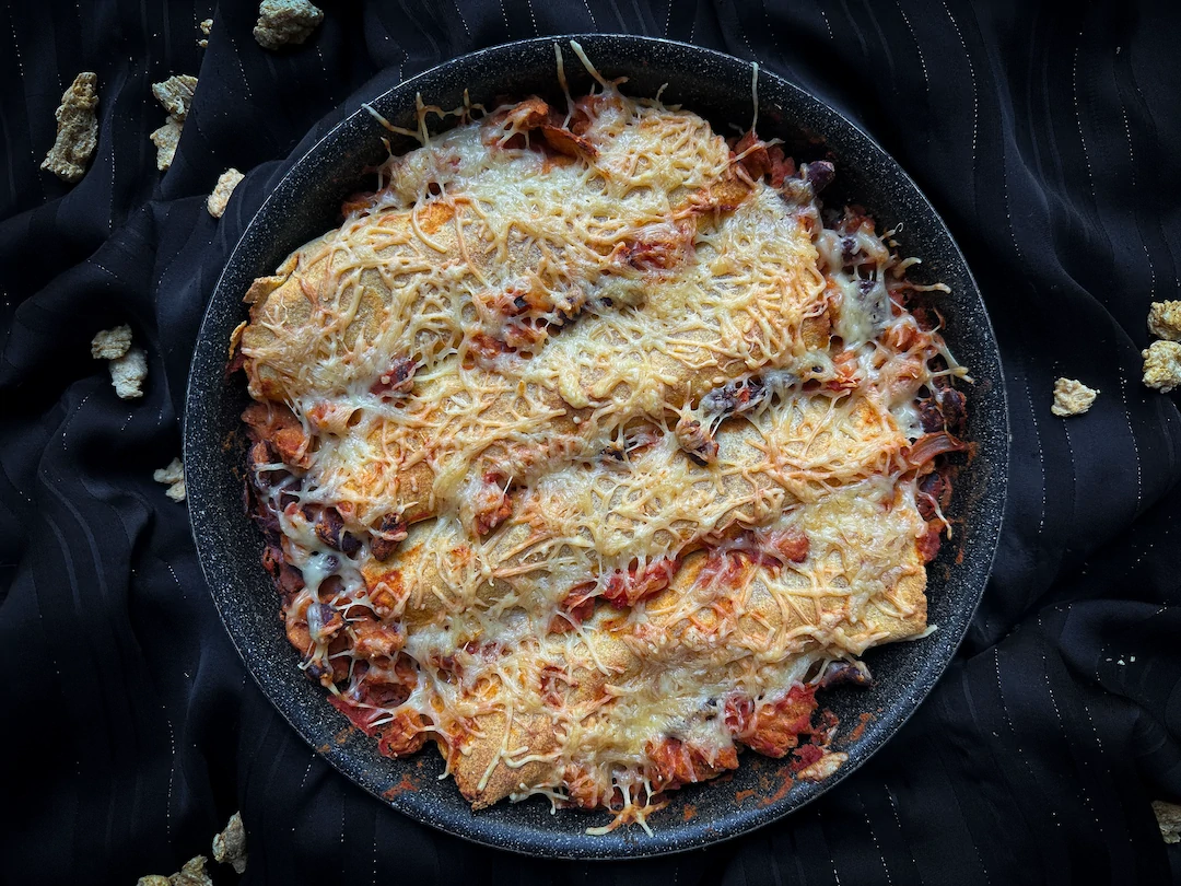These vegetarian enchiladas with cheese, kidney beans, and soy protein are presented in a black baking dish.
