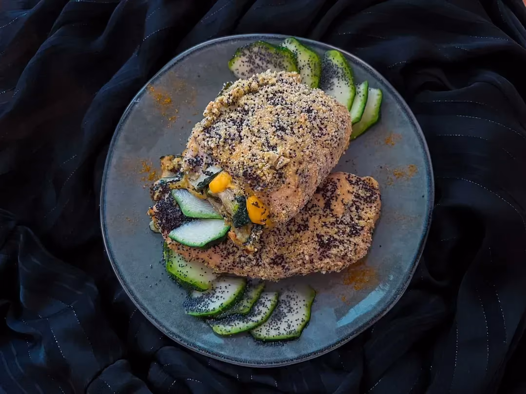In a large dark blue earthenware bowl, there are two beautiful breaded chicken cutlets with thin slices of zucchini.