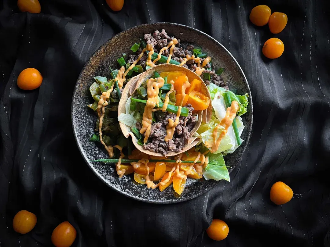 A small blue bowl serves as the setting for the fajita bowl, made with two tortillas, ground beef, bell peppers, and cherry tomatoes.