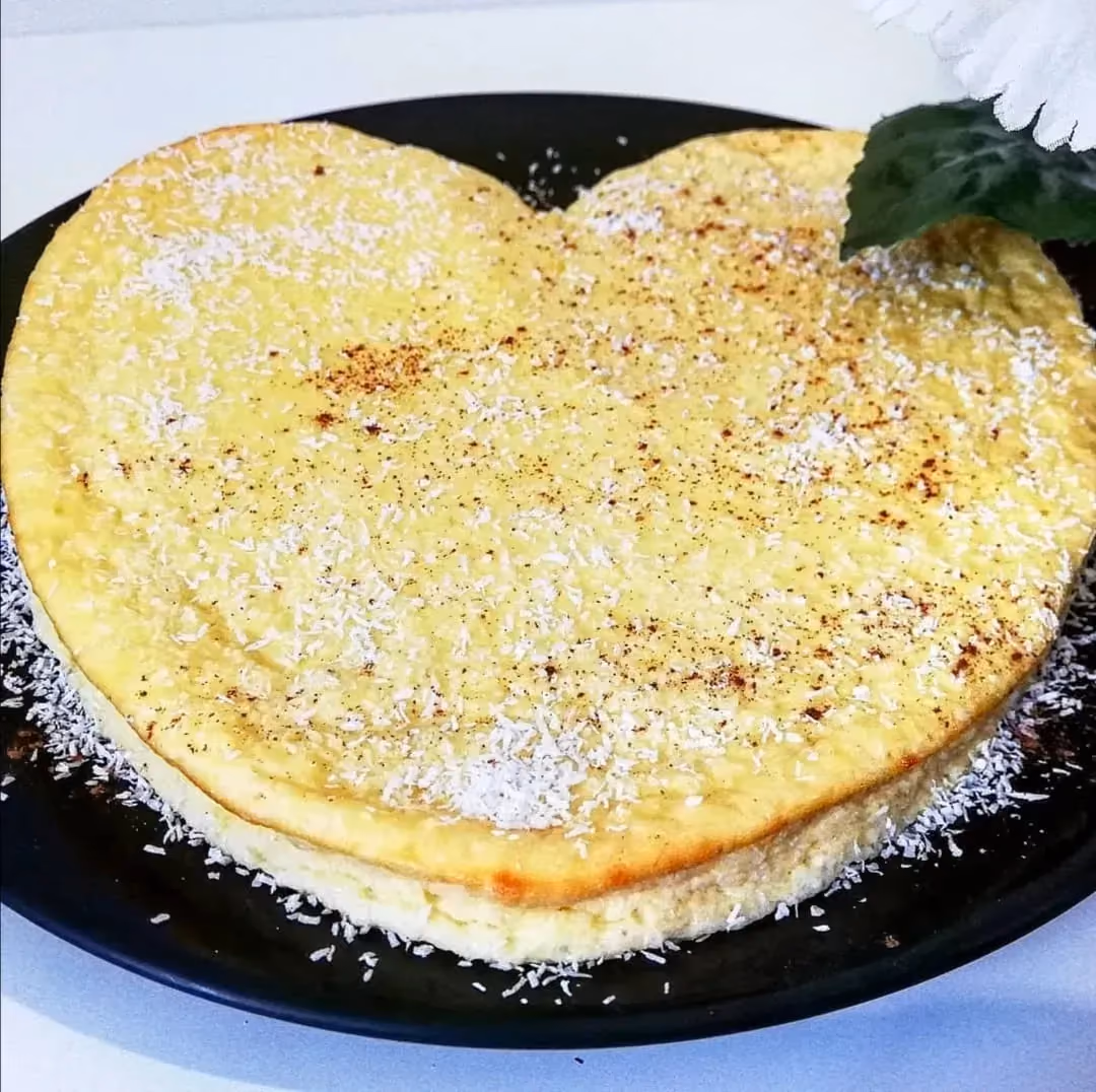 Présenté sur une grande assiette de couleur noire, le cheesecake en forme de coeur est saupoudré généreusement de noix de coco râpée.