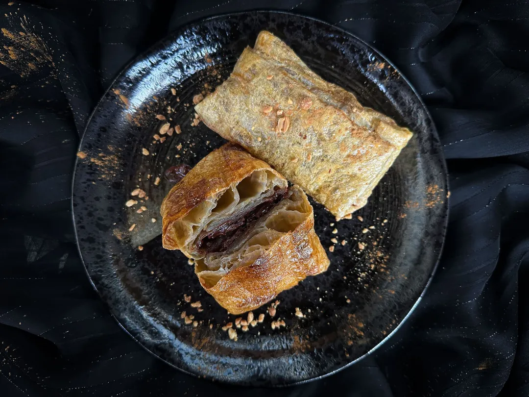 Two large pieces of chocolate puff pastry are presented in a small blue earthenware bowl.