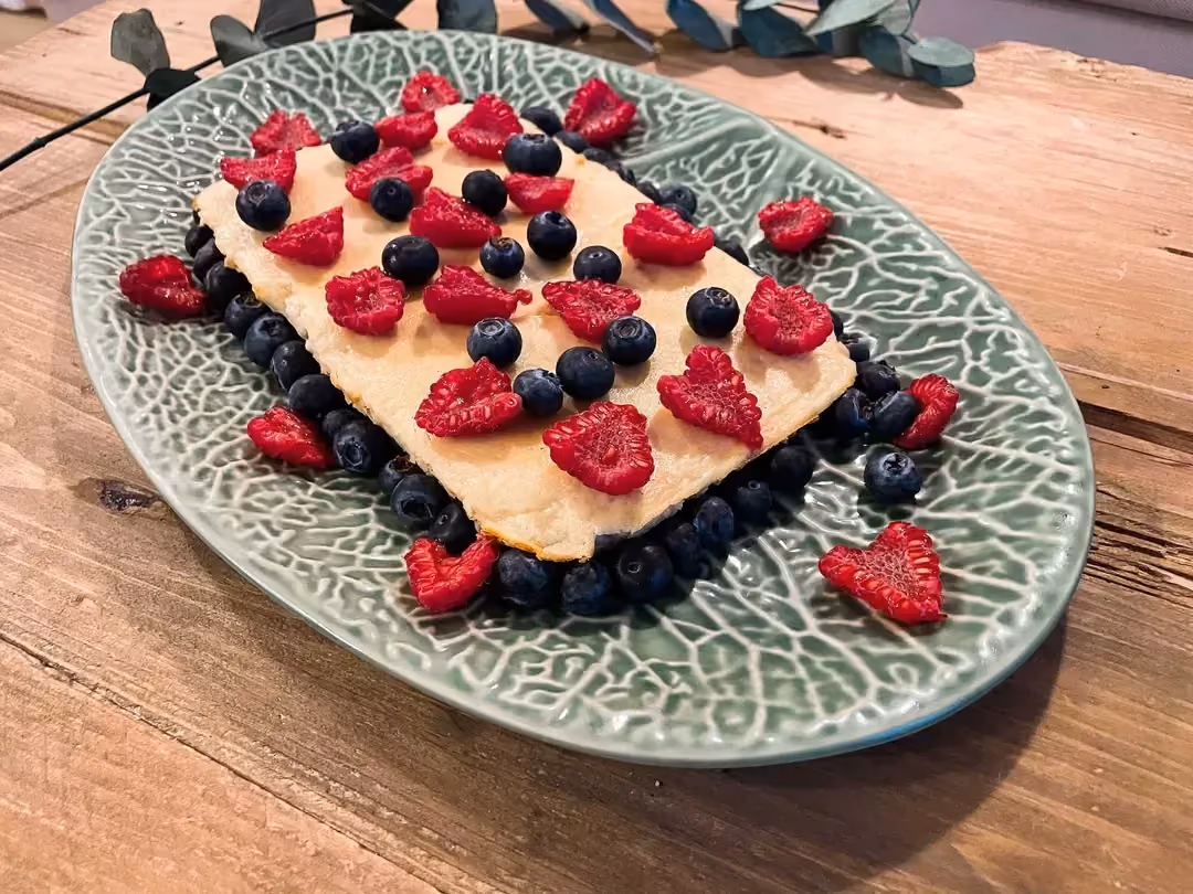 Disposé sur un plat ovale de couleur bleu et blanc, le flanc à la banane est accompagné de demis groseilles et de myrtilles.