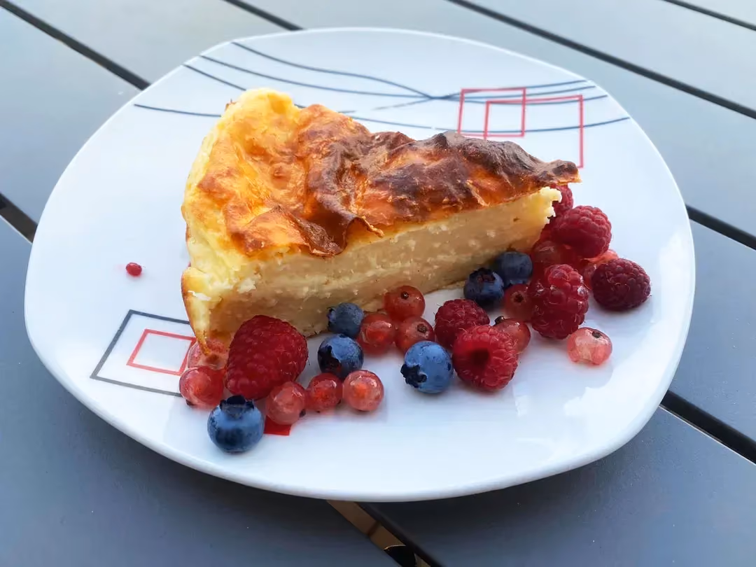 Sur une assiette de couleur blanche design se trouve une belle part de flanc pâtissier au coco accompagnée de fruits rouges