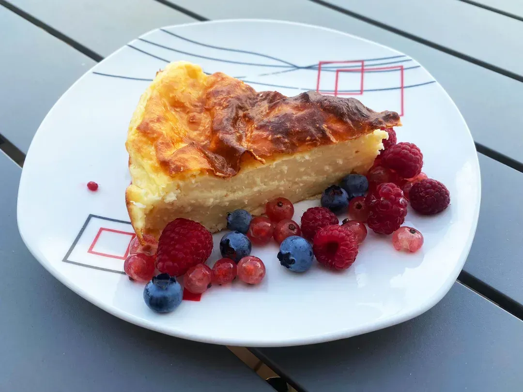 On a stylish white plate, there is a beautiful slice of coconut custard tart served with red berries