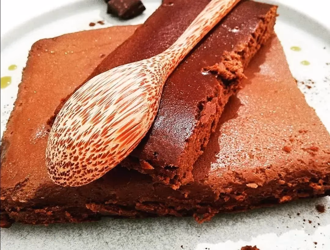 Sur un plat peu profond de couleur blanc se trouve le fondant choco et caramel. Une large part de ce dessert est déjà coupée.
