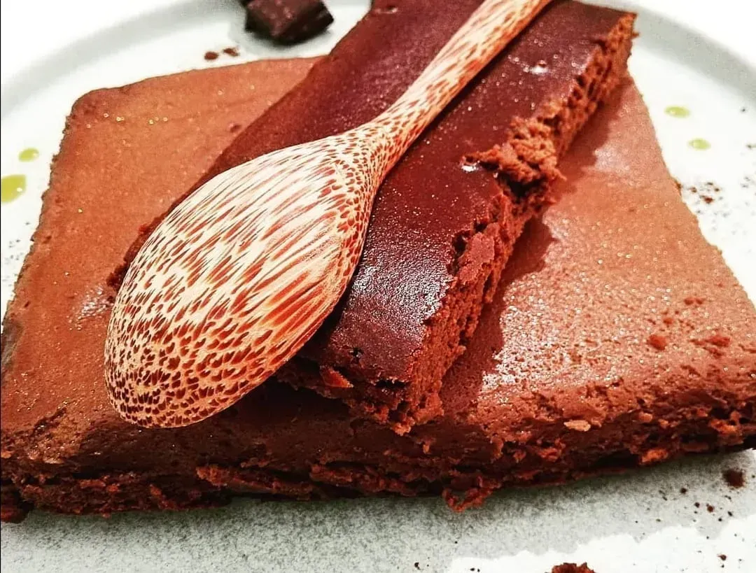 On a shallow white plate sits the chocolate and caramel fondant. A large slice of this dessert has already been cut.