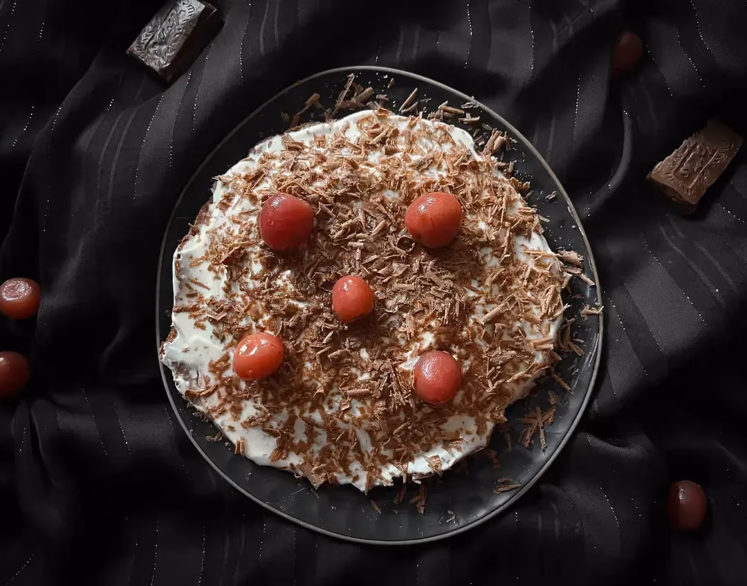 In a small blue honeycomb-patterned bowl is the Black Forest dessert. Five morello cherries are used as a topping.