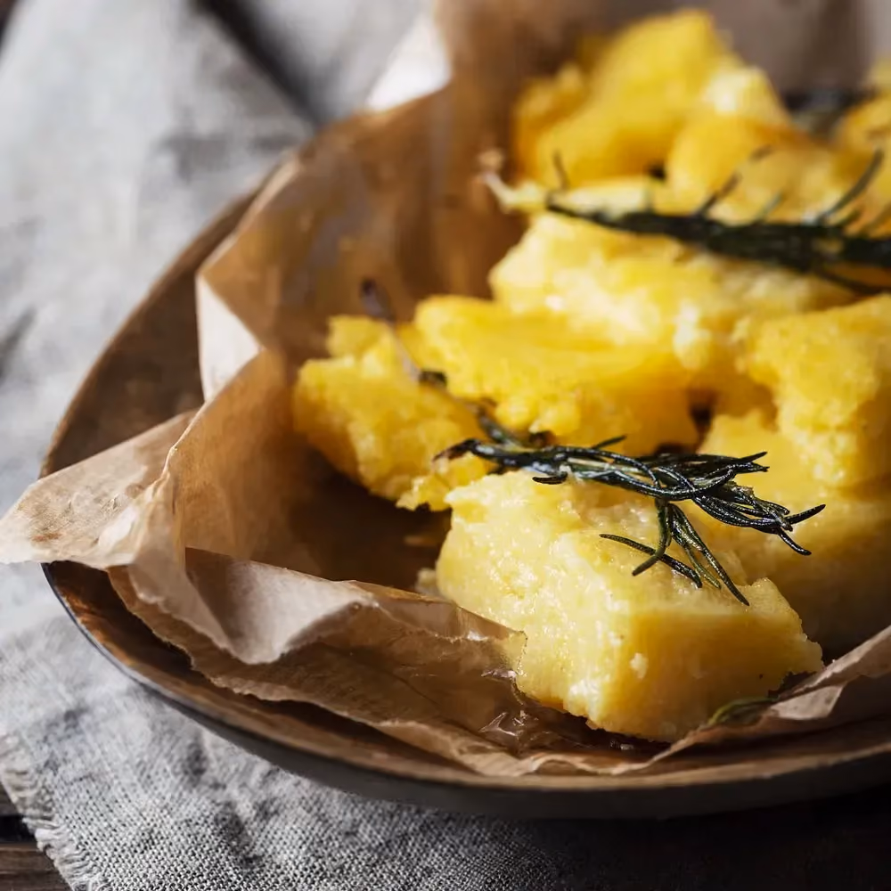 Dans un plat on retrouve de grosses frites de polenta posées sur un papier de couleur brun pour absorber l'excédant d'huile de cuisson.