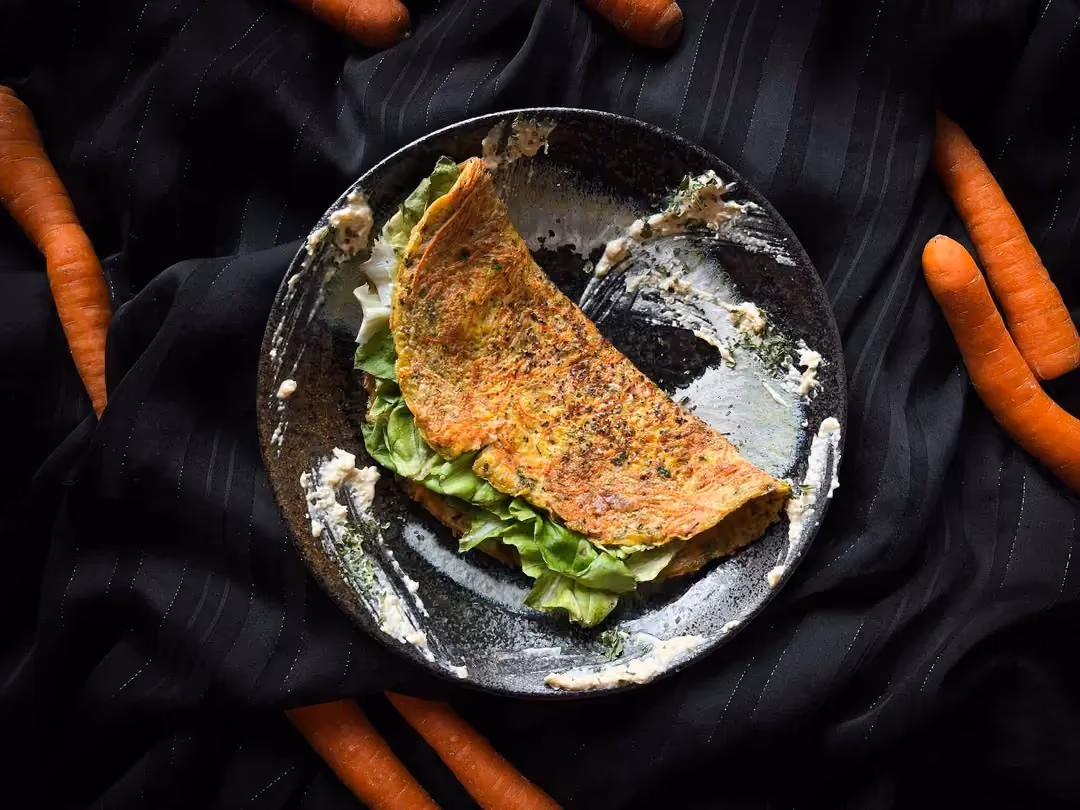 The carrot and cheese patty is presented in a small blue bowl. Seven small carrots are arranged around the bowl.
