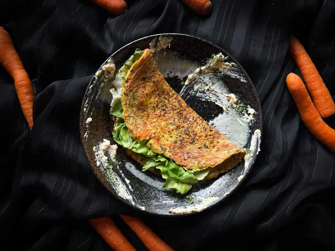 The carrot and cheese patty is presented in a small blue bowl. Seven small carrots are arranged around the bowl.
