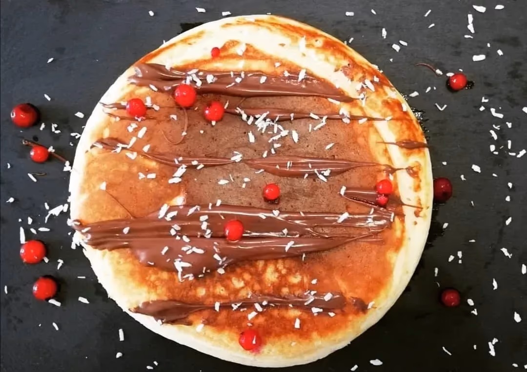 Sur une plaque de cuisson, une galette au coco bien dorée reçoit comme topping quelques petites groseilles et du coco finement râpé.