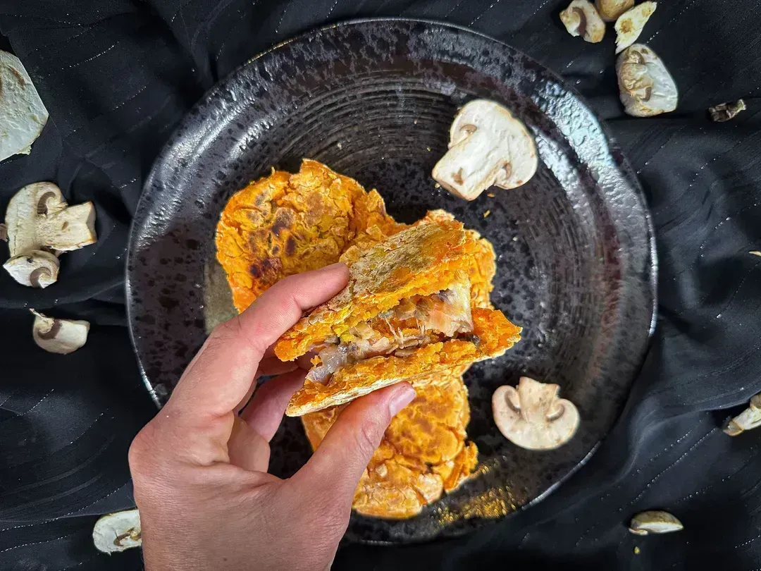 A sweet potato galette stuffed with button mushrooms and cheese is shown above a small salad bowl.