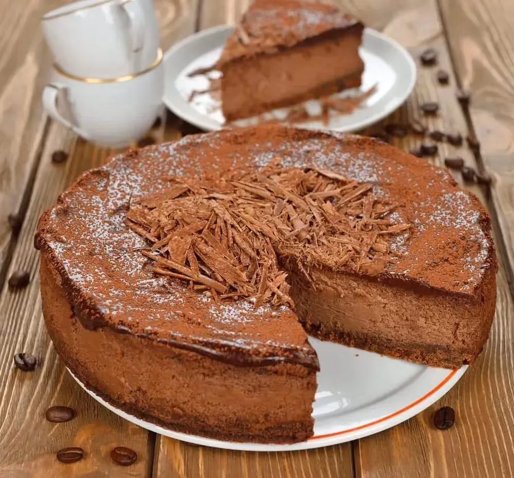 Sur une table en bois se trouve une assiette contenant un cheescake au chocolat. Une petite part est déjà prélevée et mise sur une petite assiette..
