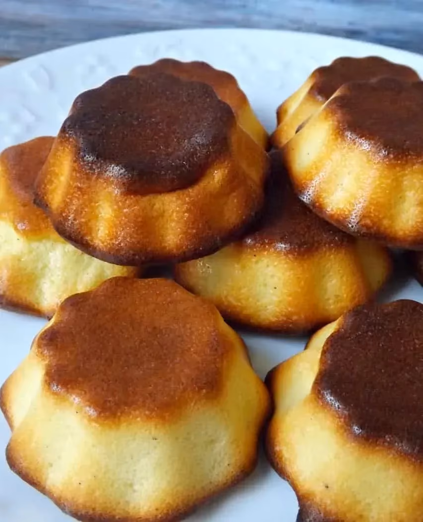 Sur une assiette blanche sont disposés six gâteaux au fromage blanc ressemblant à des cannelés bordelais