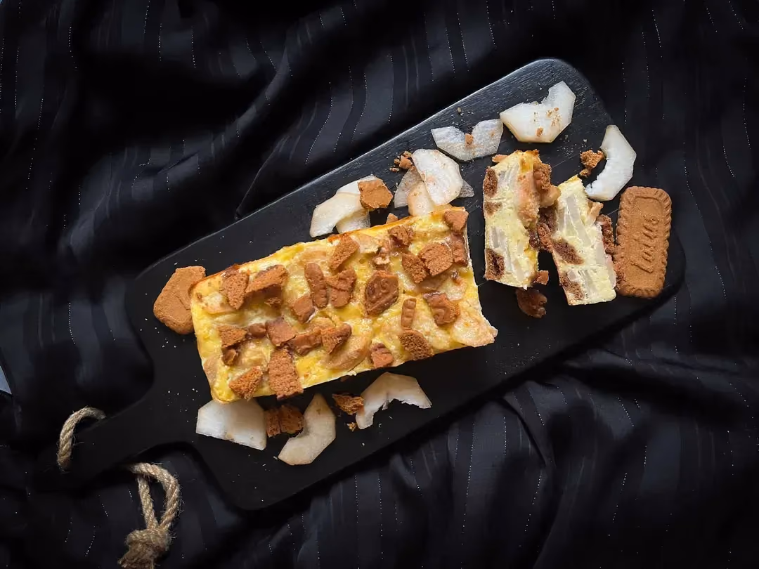 Le gâteau protéiné aux poires et spéculoos est présenté sur une sorte de planche à découpée de couleur noire.