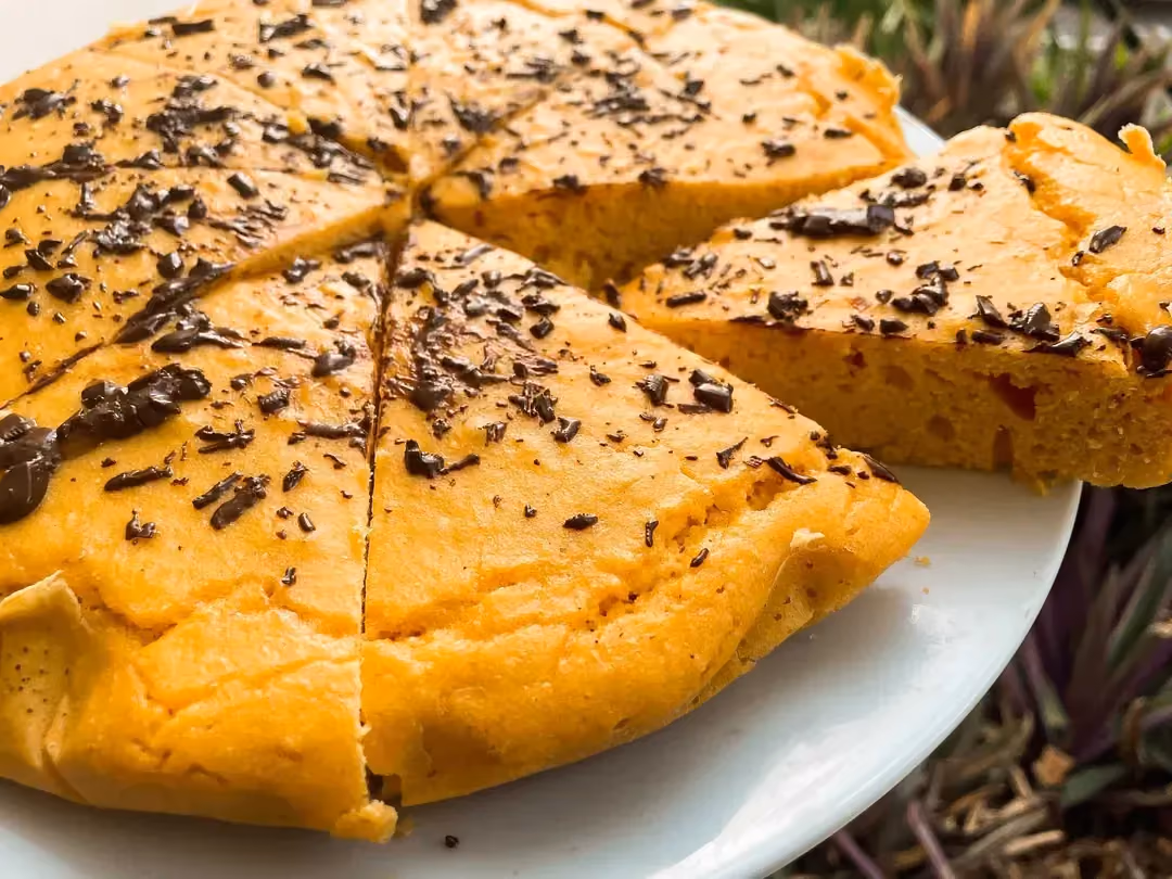 Le gâteau à base de farine de maïs est coupés en huit parts et saupoudrés de chocolat émietté présenté dans une assiette de couleur blanche.