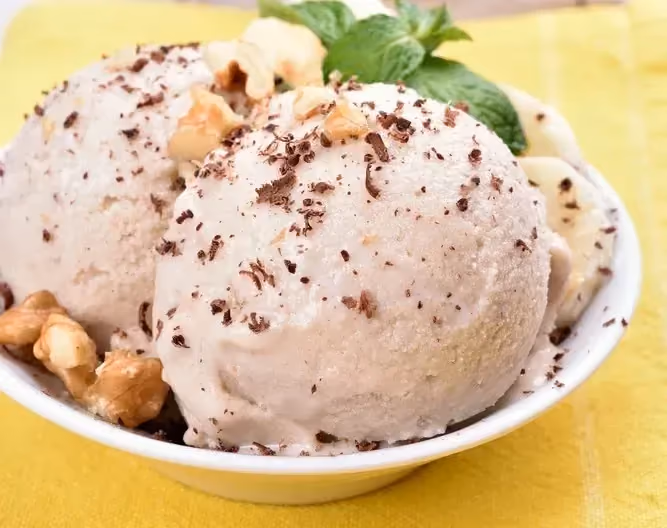 Un petit saladier de couleur blanc accueille deux grosses boules de glace, de la banane coupée en tranches et une feuille de menthe.