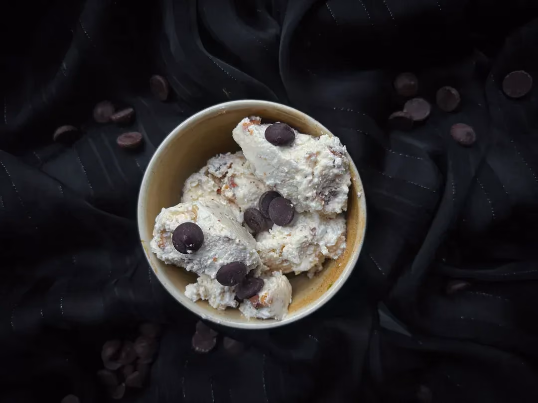 Dans un bol en grès de couleur beige, se trouve la glace cottage cheese et la purée de cacahuètes. Les pépites de chocolat constitues le topping.