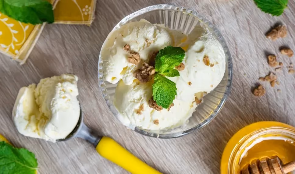 Dans un bol en verre se trouve la glace à la vanille et au miel avec une petite feuille de menthe dessus. Dans un autre bol se trouve le miel.