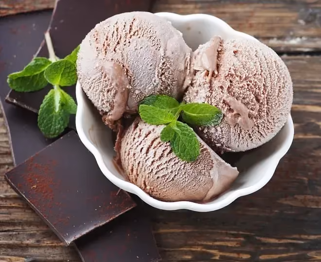 Dans un joli bol au bord ourlé, se trouve trois grosses boules de glace, avec une petite feuille de menthe comme topping.