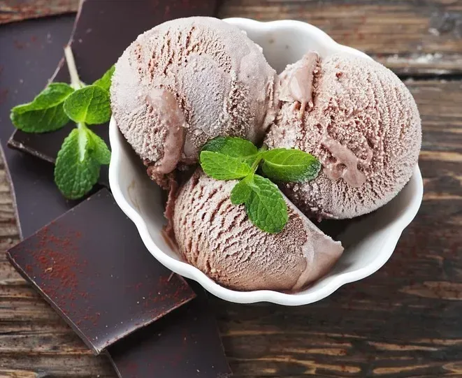 In a pretty bowl with a scalloped rim, there are three large scoops of ice cream, topped with a small mint leaf.