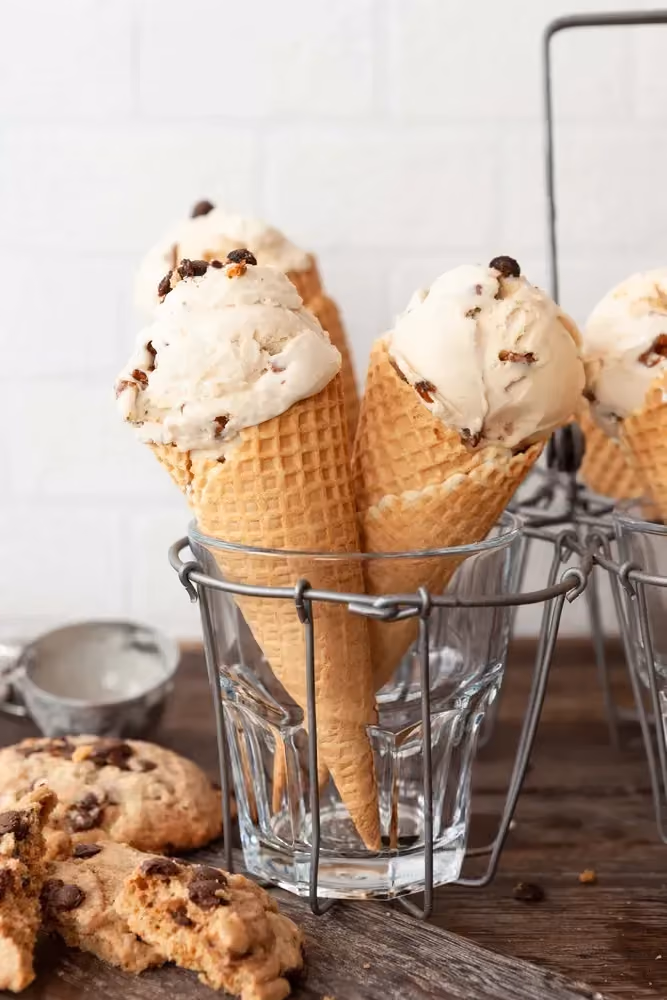 La glace à la vanille et cookies est présentée dans des cornets traditionnels. Deux cookies accompagnent les cornets de glace.