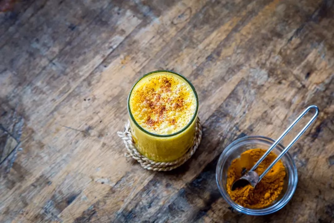 Sur une table en bois rustique, on retrouve une verrine remplie de "golden milk" et un pot contenant du curcuma.