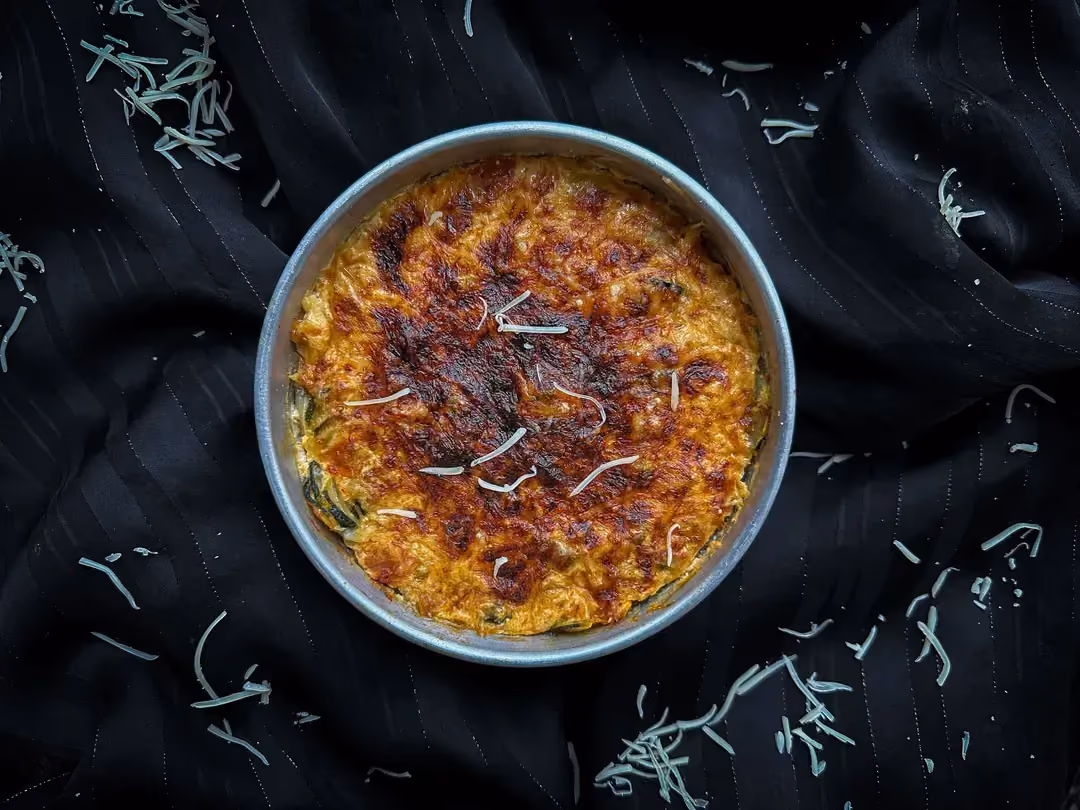 Le gratin de courgettes végétarien est présenté dans un grand plat à gratin . Les courgettes coupées en rondelles sont enrobées de fromage râpé.