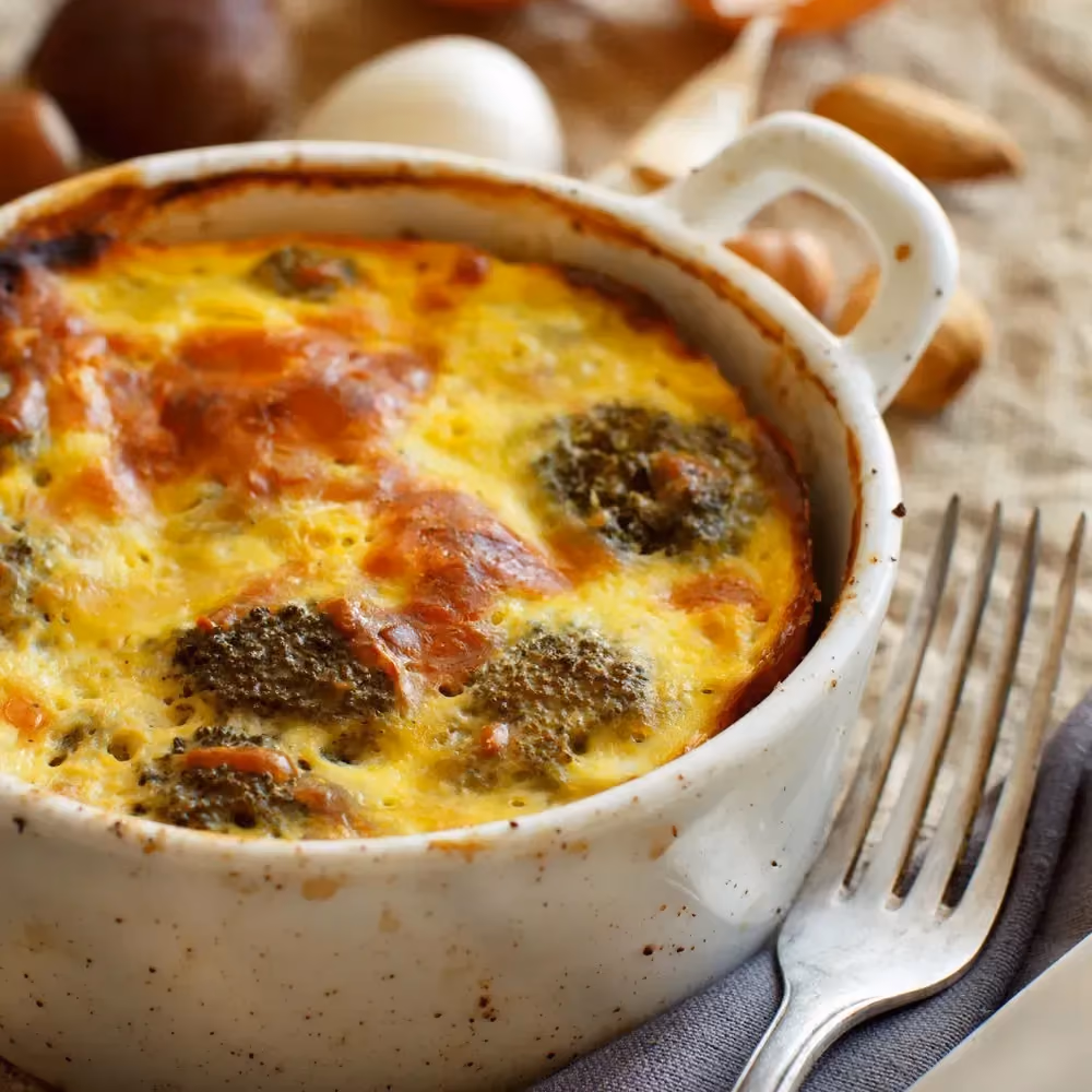 Broccoli gratin with turkey ham is presented in a round white stoneware baking dish.