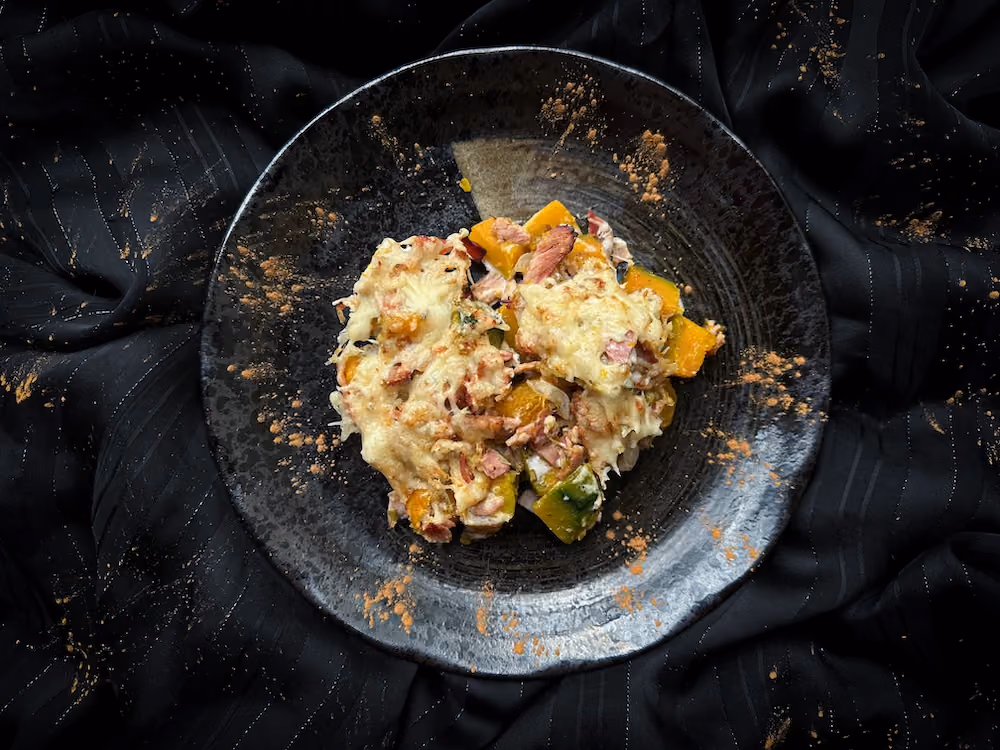This squash gratin is presented in a white earthenware charlotte mold. On top is grated cheese and a silver pie server.