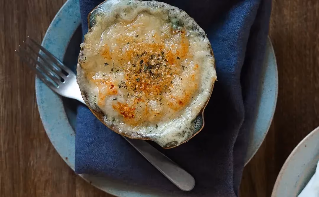 Chayote gratin is topped with a layer of grated cheese and served in small blue ramekins.