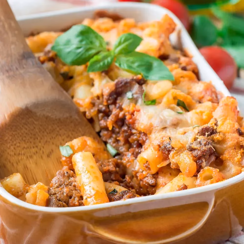 In a square baking dish with rounded corners, the baked bolognese pasta shows ground beef and red lentil pasta.