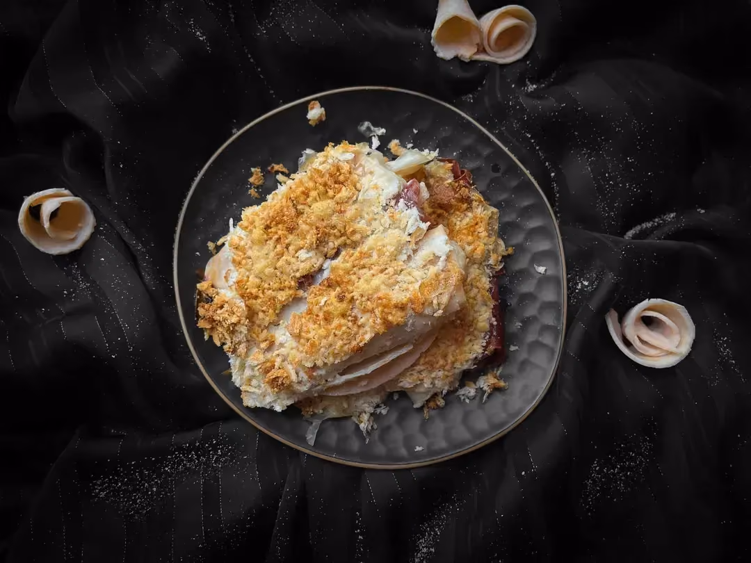 The endive gratin with turkey breast and viande des Grisons, sprinkled with grated cheese, is presented in a blue honeycomb-patterned dish.