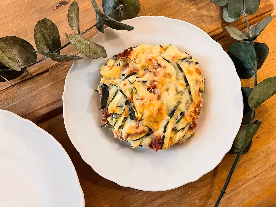Présenté dans une assiette creuse de couleur blanche, disposée sur une table en bois clair, ce gratin semble très appétissant.