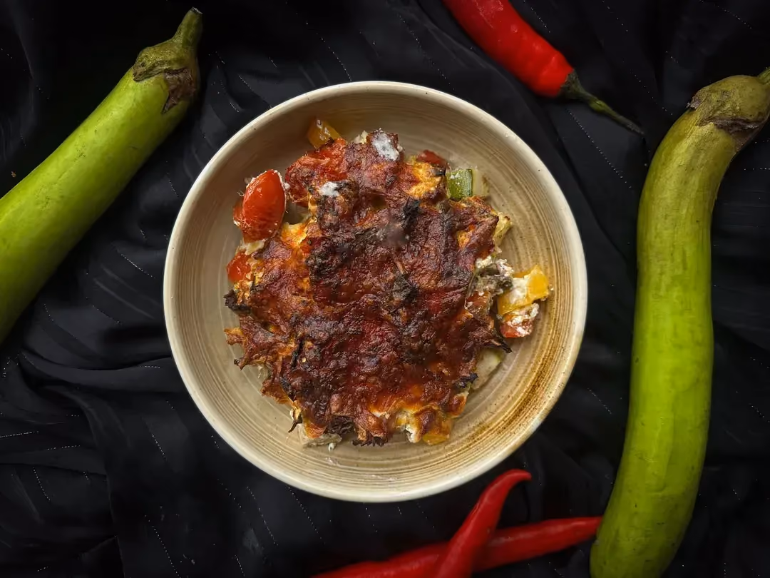Une personne avec un tablier de cuisine vient de prélever une grosse part de gratin au thon pour la déposer sur une assiette de couleur noire..