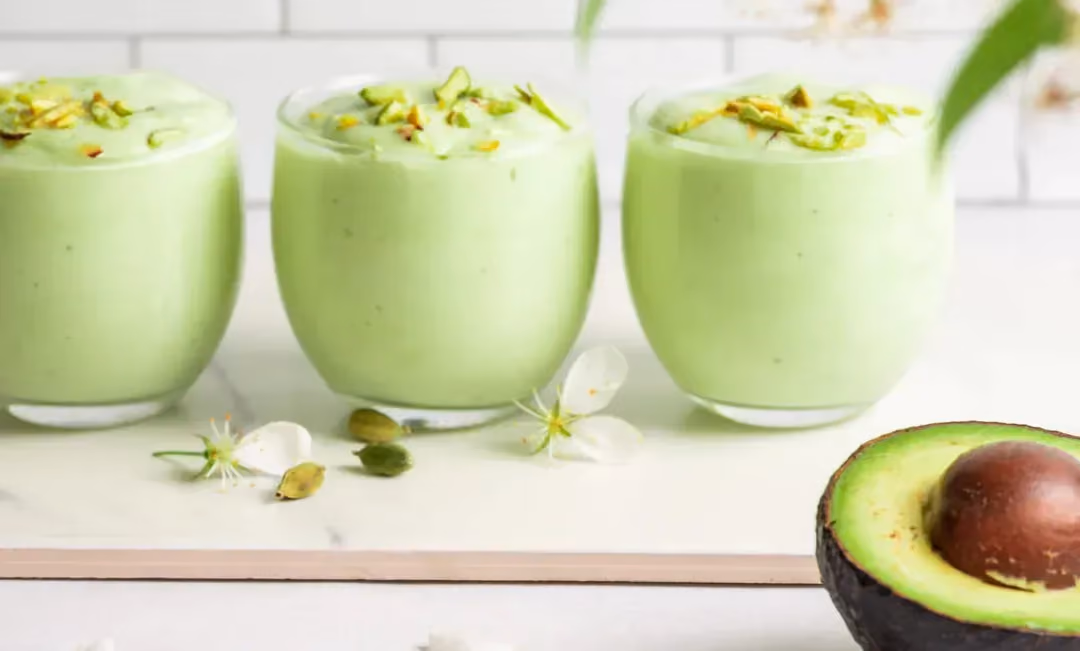 Three verrines are filled with the pale green "Green Hulk" mixture. Half an avocado with its pit is placed beside them.