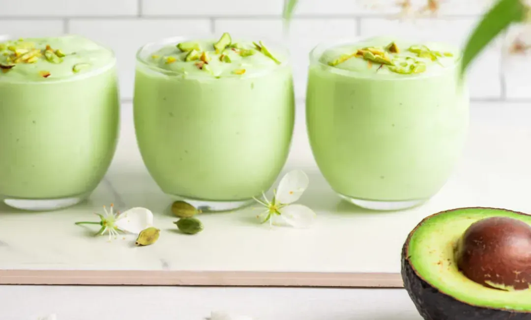 Trois verrines sont remplies de la préparation "Green Hulk" à la couleur vert tendre. Un demi avocat avec son noyau se trouve à côté.
