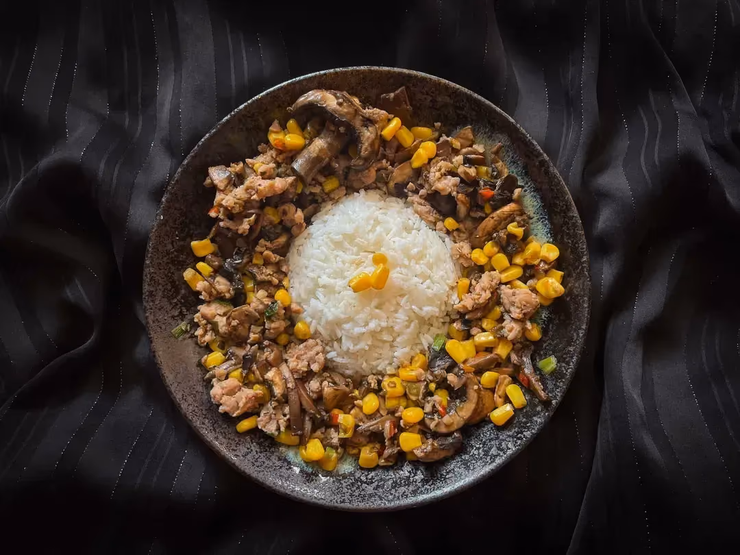In a small blue bowl are the ground chicken, button mushrooms, and corn with two peppers.