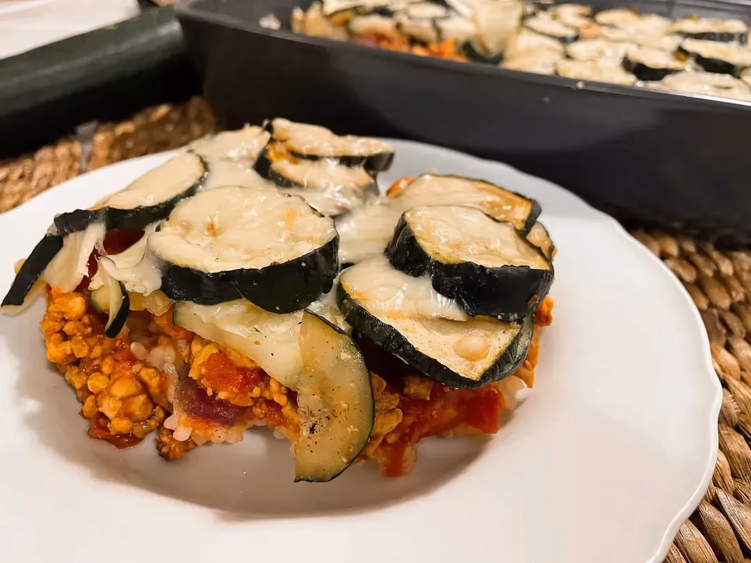 On a bed of red-colored rice thanks to the tomatoes, the minced meat is layered on top, and finally the zucchini cut into thick slices.
