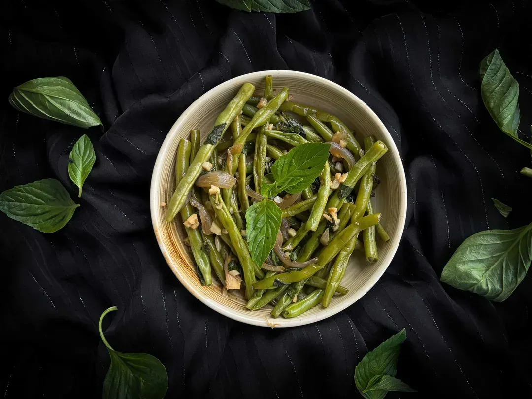In a white earthenware dish, the green beans with garlic and parsley are ready to eat. Two forks are visible.