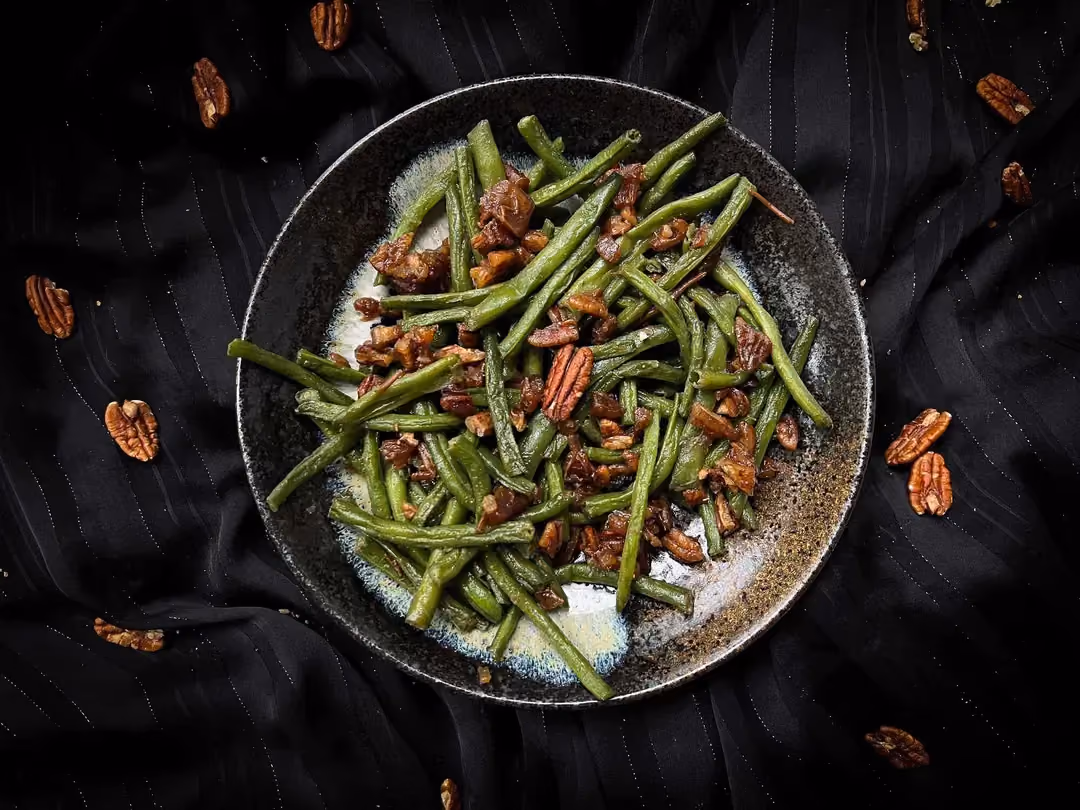 La recette de haricots verts aux noix de pécan caramélisées et dattes est présentée dans un petit saladier de couleur bleu.